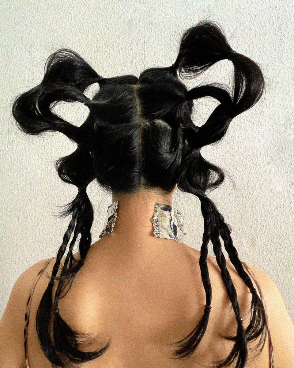 Artistic hair design titled '阿修羅' by Taiga Sato, featuring intricate black hair styling with sculptural loops and braids. The model is adorned with textured silver accessories on the neck, creating a striking visual contrast. Captured from the back, highlighting the symmetrical hair arrangement.