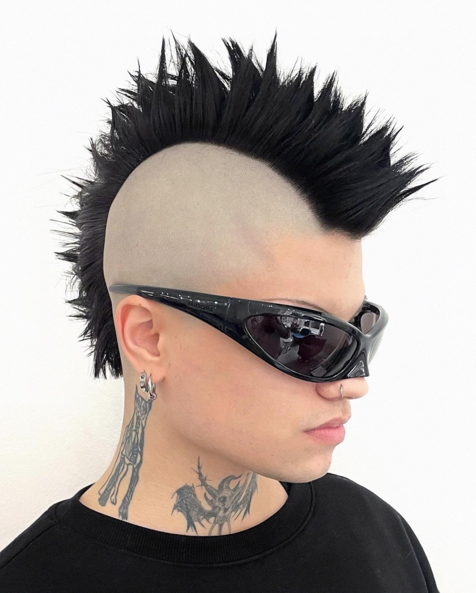 Side profile of Barbie Drugz with a bold mohawk hairstyle, cleanly shaved sides, styled by Taiga Sato. The model wears futuristic black sunglasses and showcases neck tattoos.